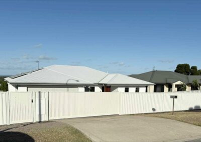 White single-story home behind a tall white fence with a matching gate on a sunny day
