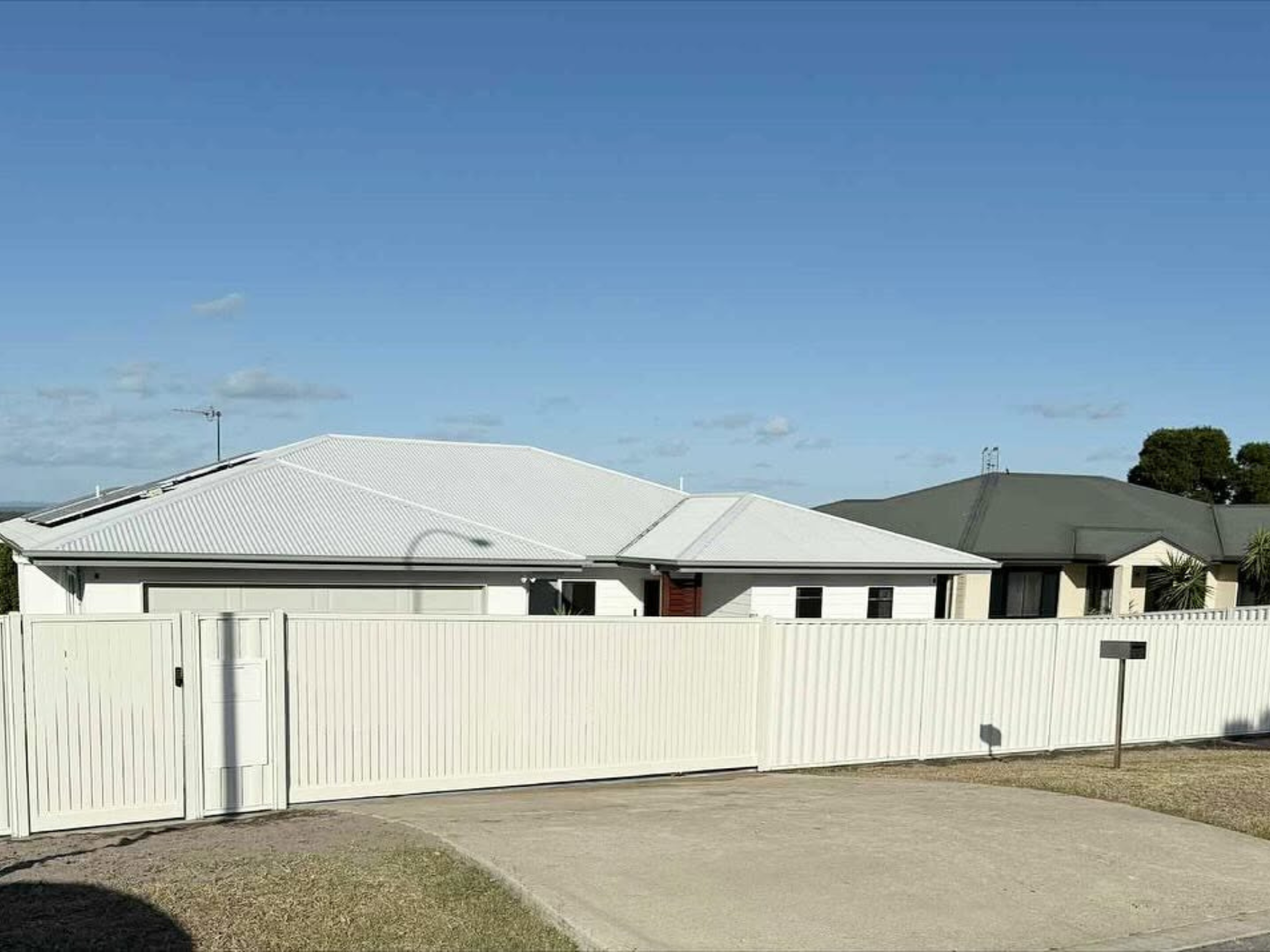 Row of white fenced houses with metal roofs under a clear blue sky.