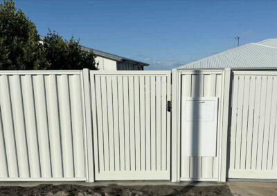 White vinyl privacy fence with a central gate and a small utility cabinet mounted on the right panel, under a clear blue sky.