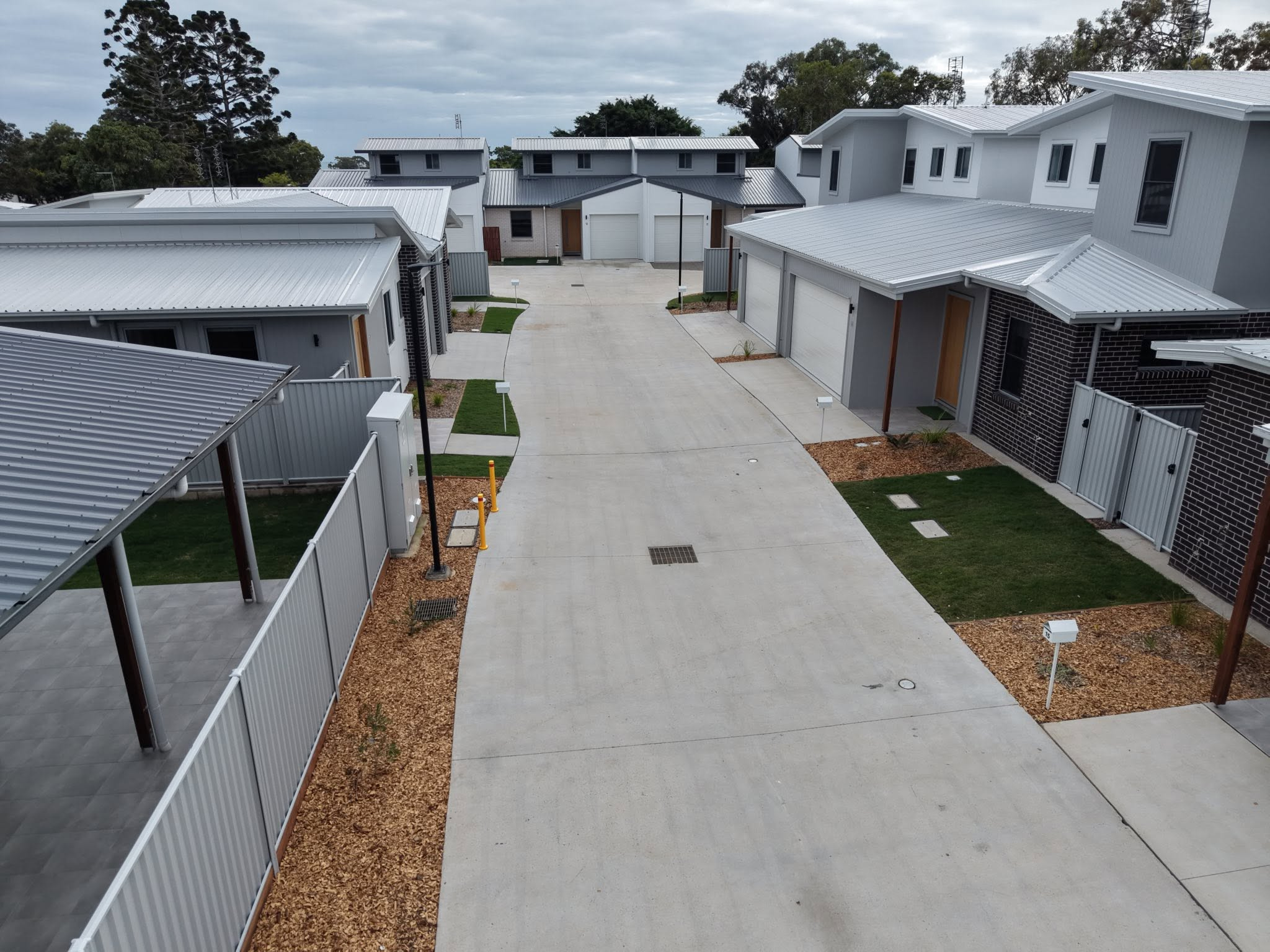 Aerial view of a modern townhouse cul-de-sac with gray metal roofs, white walls, garages, and landscaped patches.