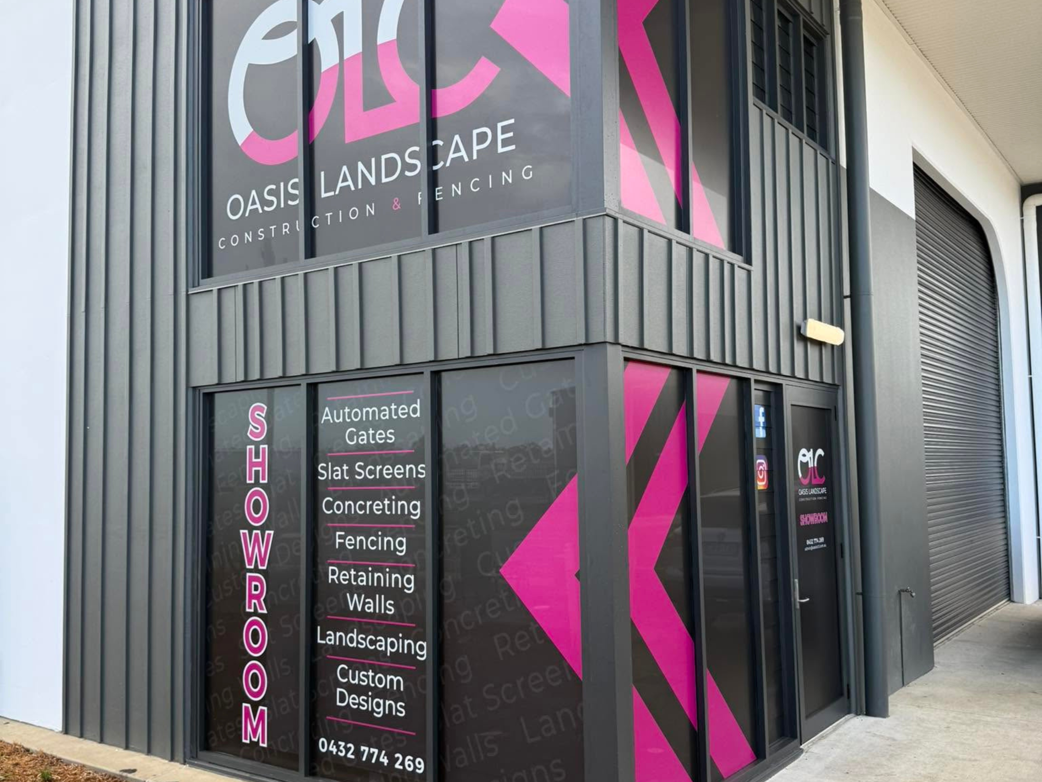 Storefront signage for Oasis Landscape with bold pink diagonal stripes on dark panels; window ads list landscaping services such as fencing, gates, walls, and custom designs.
