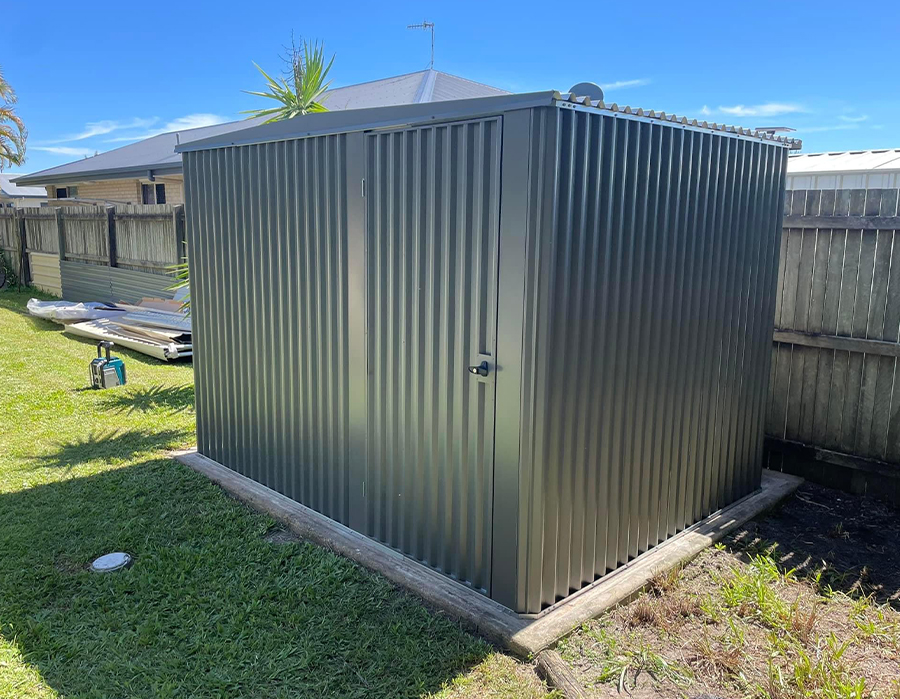 Grey Colorbond garden shed with double doors on a timber-edged slab in a backyard, installed by Oasis Landscape Construction and Fencing in Hervey Bay.